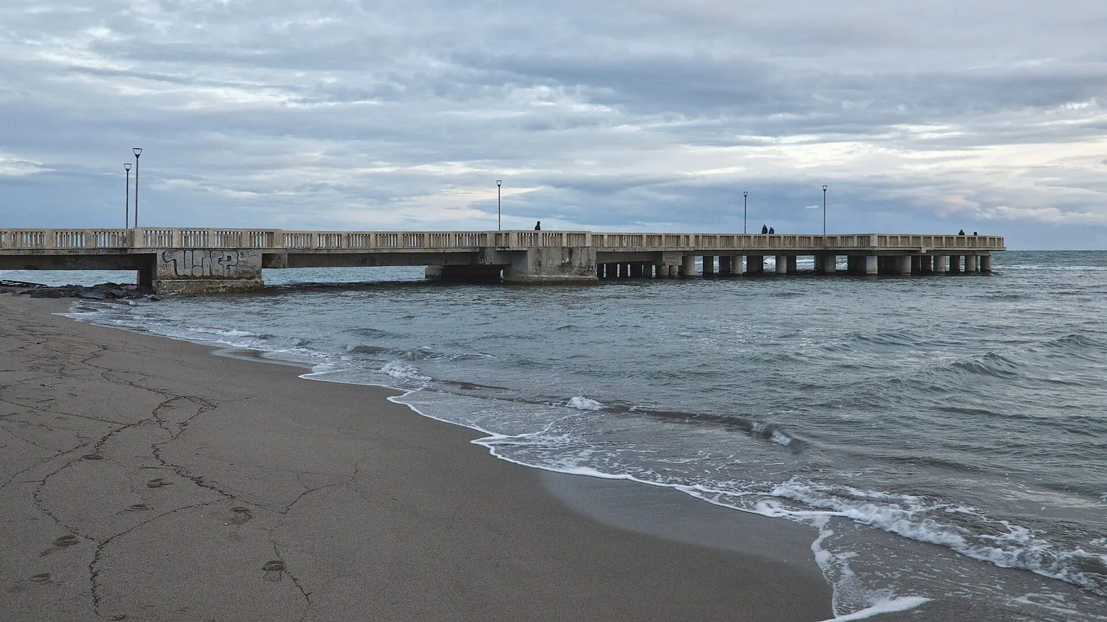 Il Pontile di Ostia visto dalla spiaggia, con il mare mosso e il cielo nuvoloso